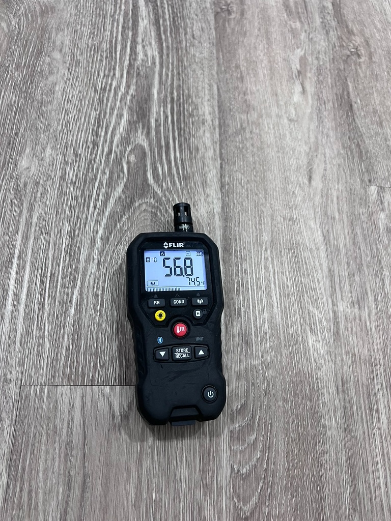 FLIR MR59 moisture meter placed on a hardwood floor showing a 56.8 percent moisture reading