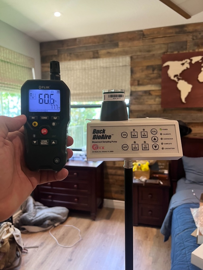 FLIR moisture meter held in a bedroom during the inspection, displaying a reading of 60.6 percent relative humidity and 77.7 degrees Fahrenheit