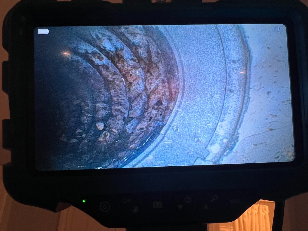 Borescope camera view of the interior of an HVAC duct or vent, showing visible debris buildup and dark staining along the duct wall