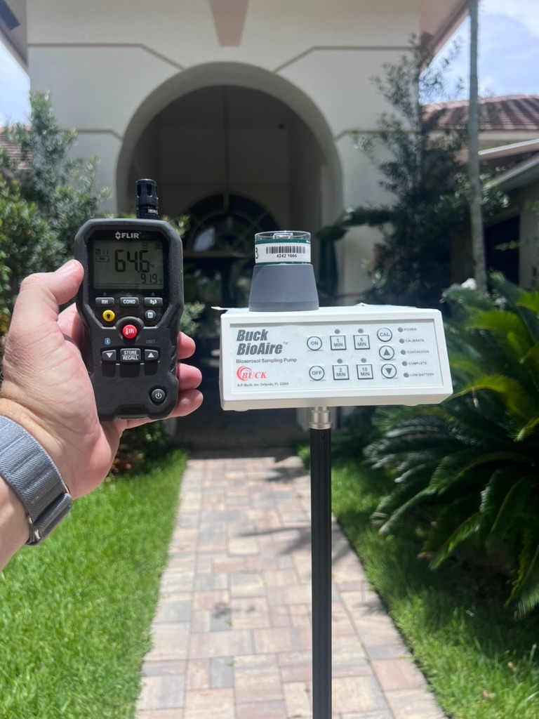 Buck BioAire air sampling pump set up outdoors in front of a residence, with a FLIR meter reading 64.6 percent relative humidity and 91.9 degrees Fahrenheit