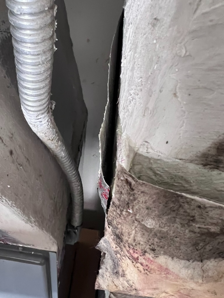 Close-up of a visible gap between two duct sections where the sealant and tape have separated, showing a dark opening between the sections