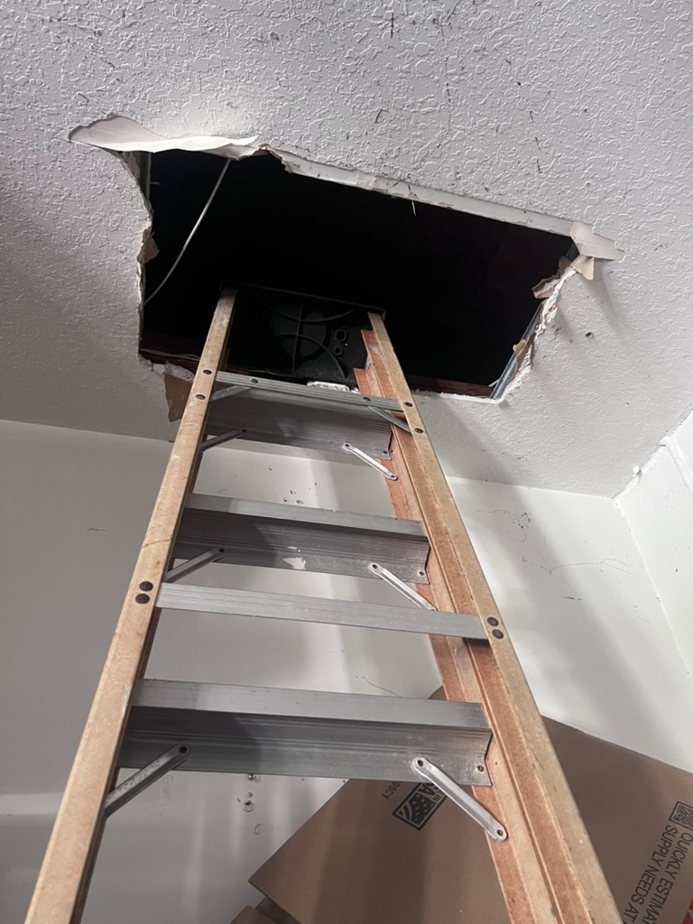 A ladder positioned beneath an open attic access hatch in a ceiling, showing the entry point used to inspect the attic and HVAC duct space